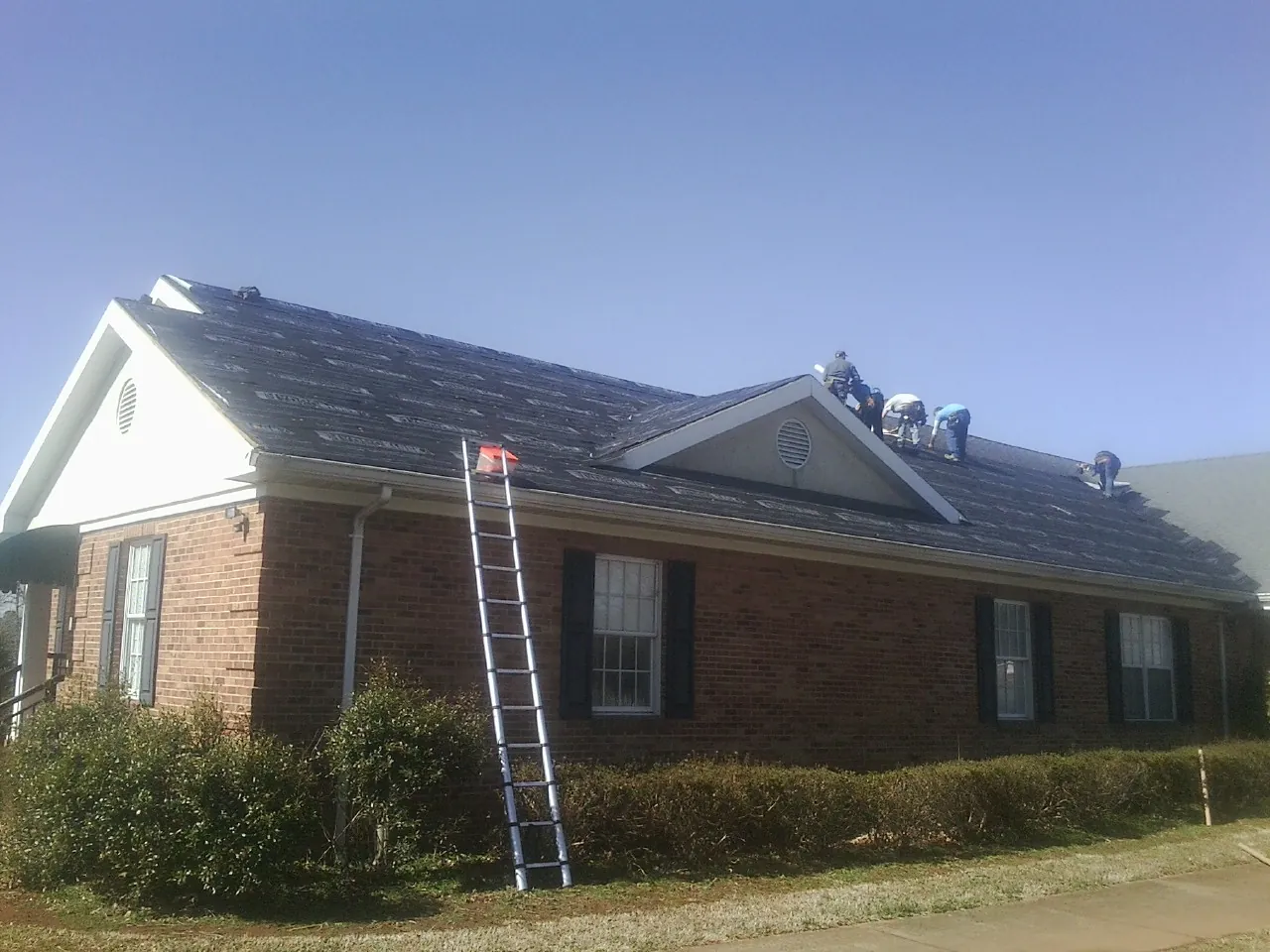 Crew tearing shingles off a brick ranch roof with a ladder set — Metal Roof Repair work by our crew in Boyertown