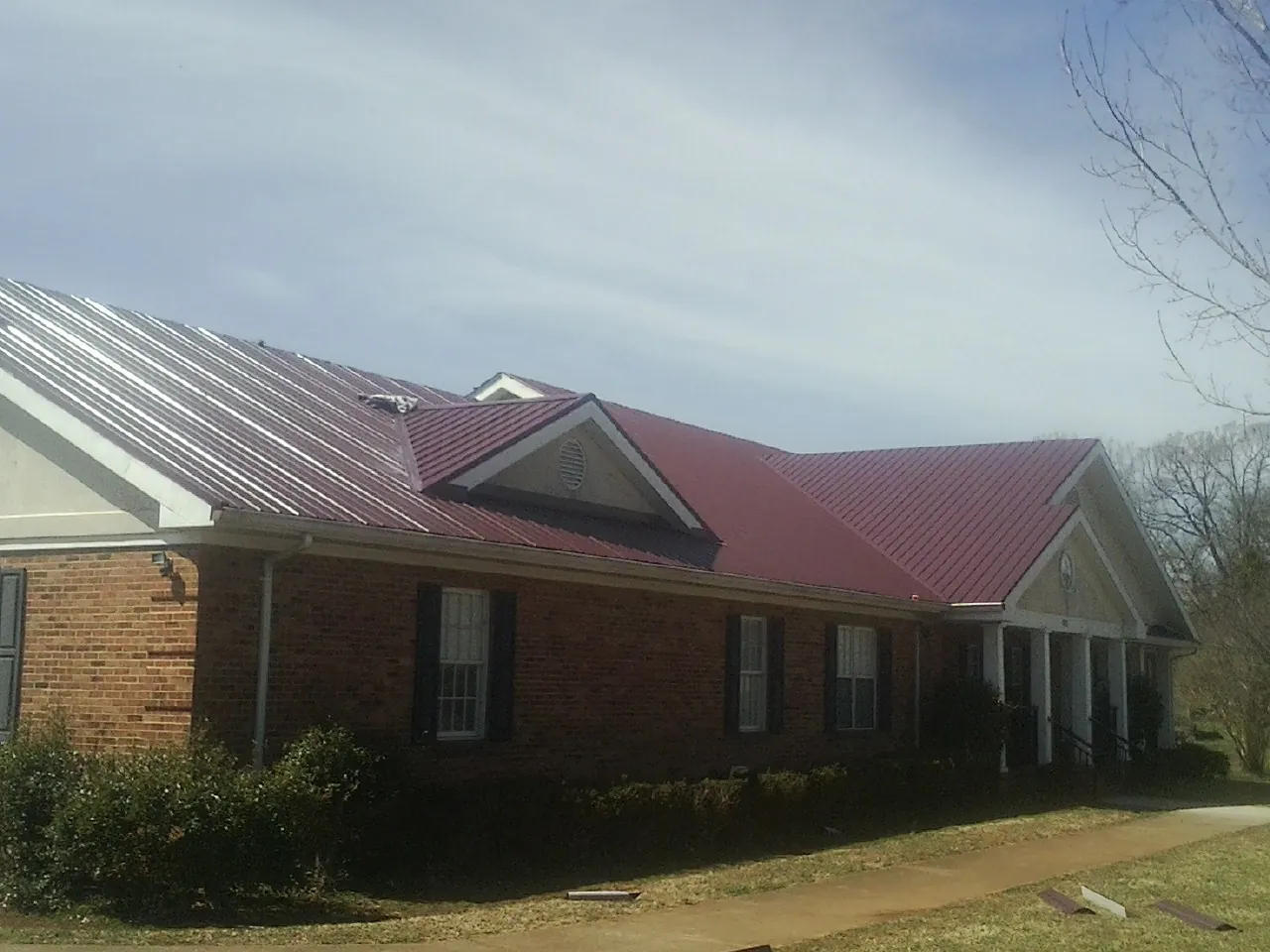 Red metal roof with gabled entries on a long brick building, from a Hail Damage Roof Repair job in Boyertown