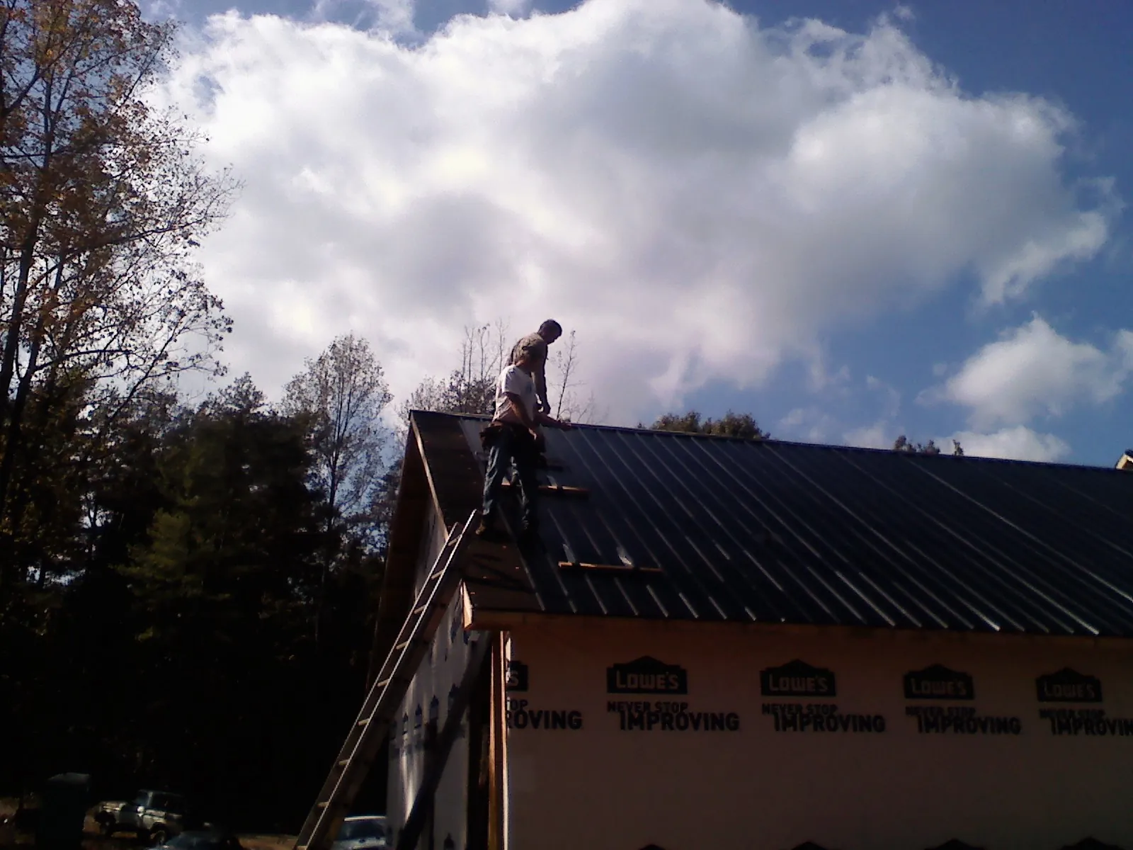 Roofer fastening dark metal panels high against a cloudy sky, from a Roof Inspection job in Boyertown