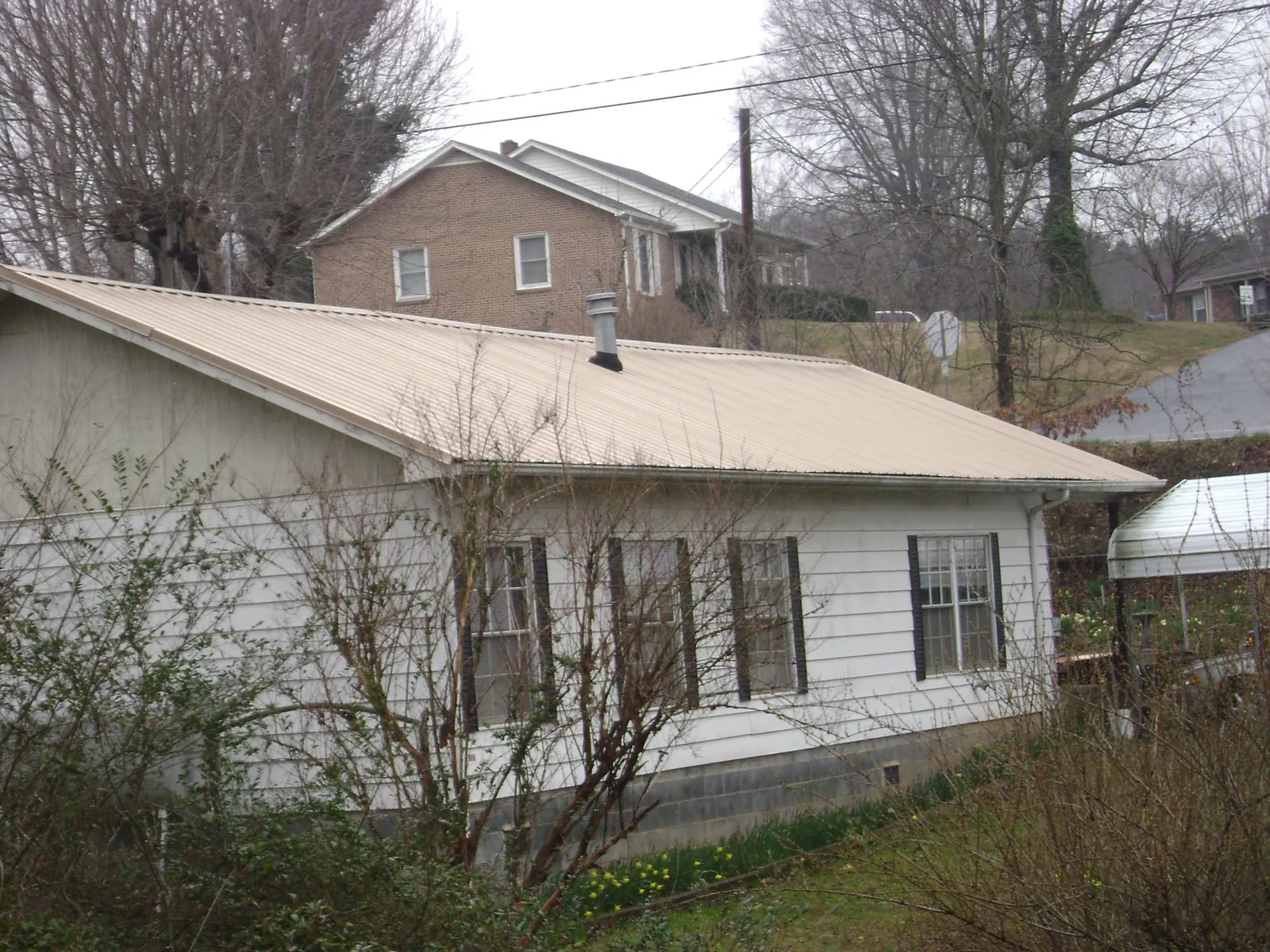 Tan metal roof on a white sided house set into a hillside — Commercial Roofing by Roofing Brothers in Boyertown